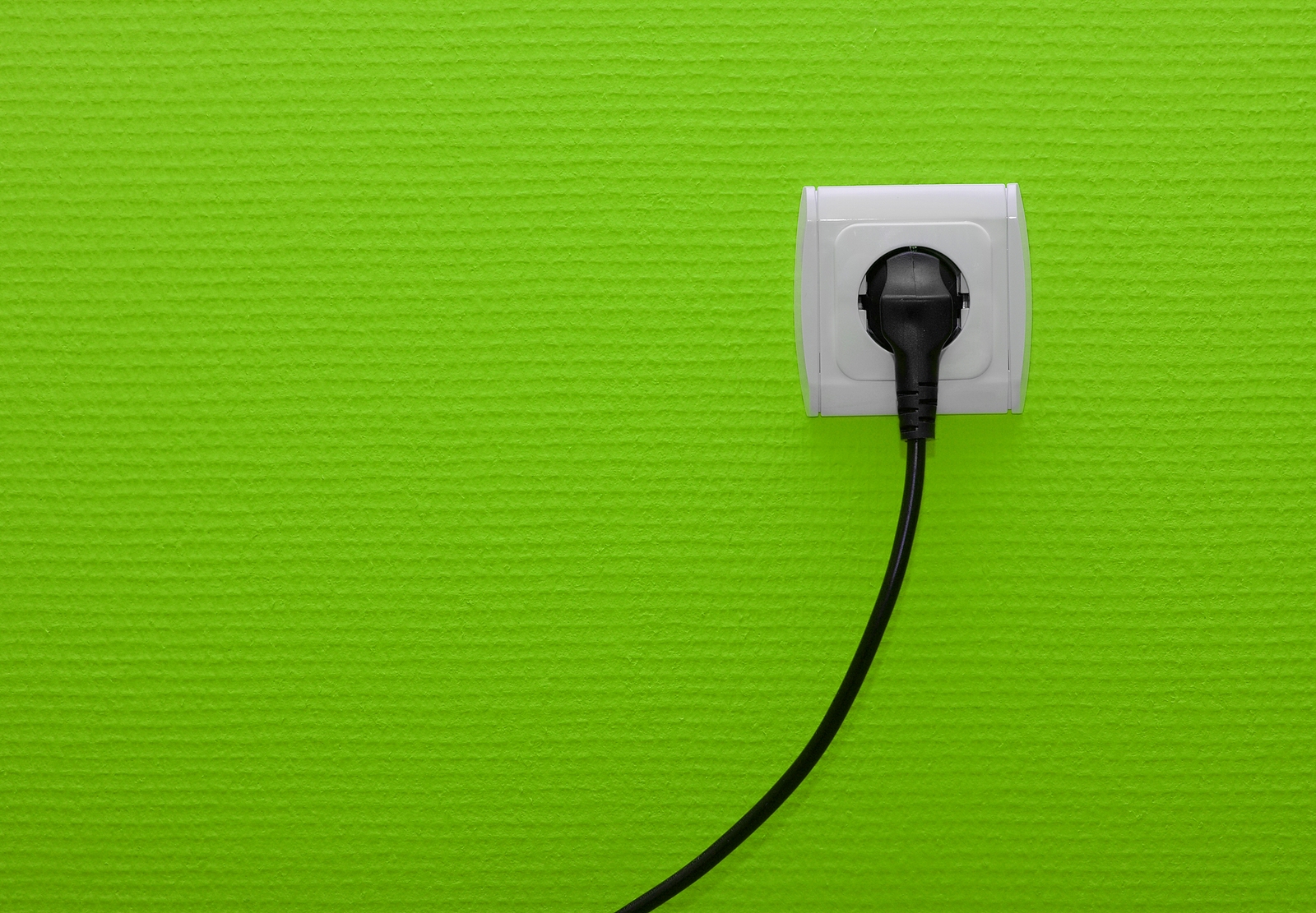 Electric outlet on green wall with cable plugged